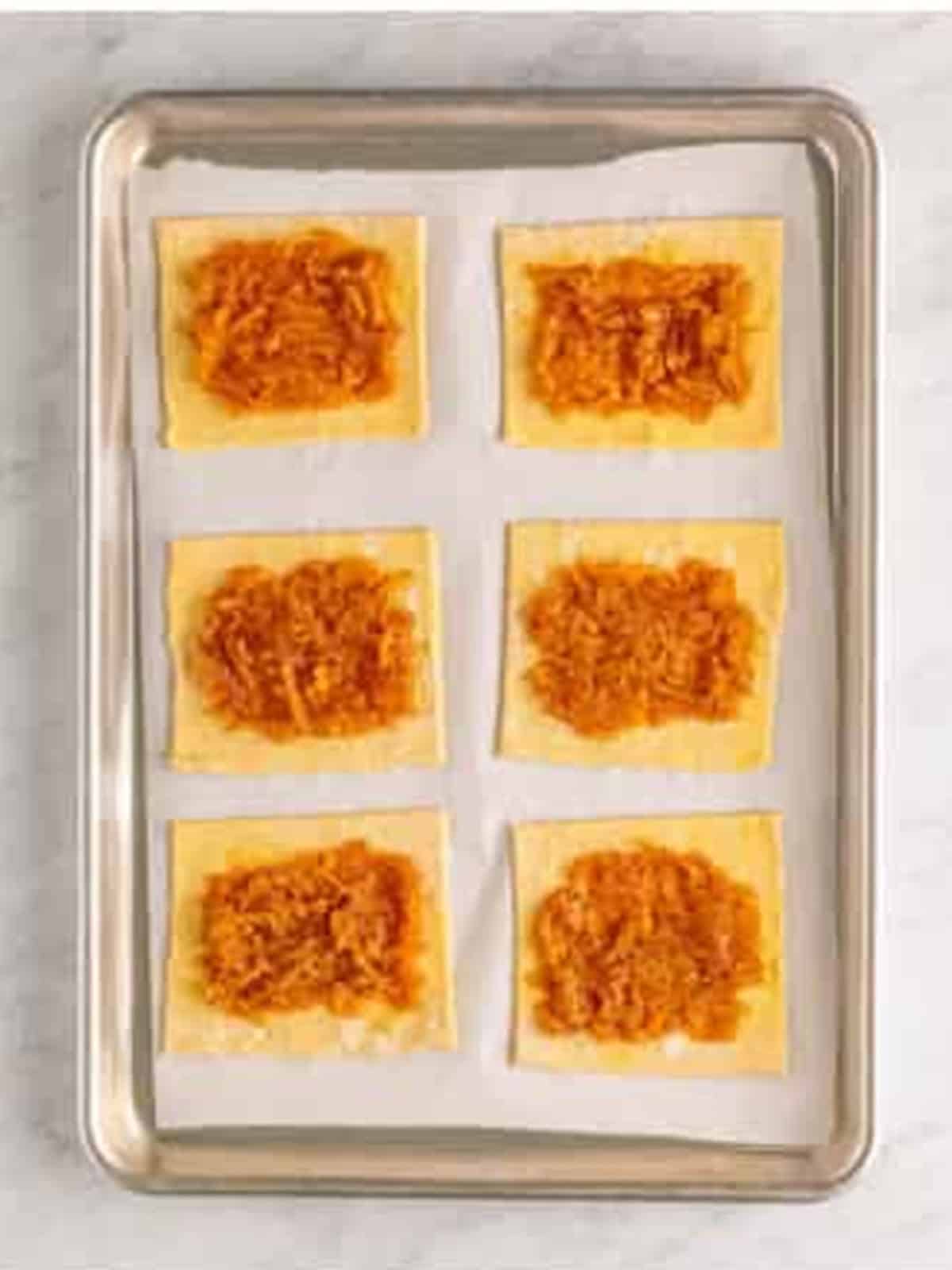 Apple filling spread over the centers of puff pastry rectangles on a sheet tray.