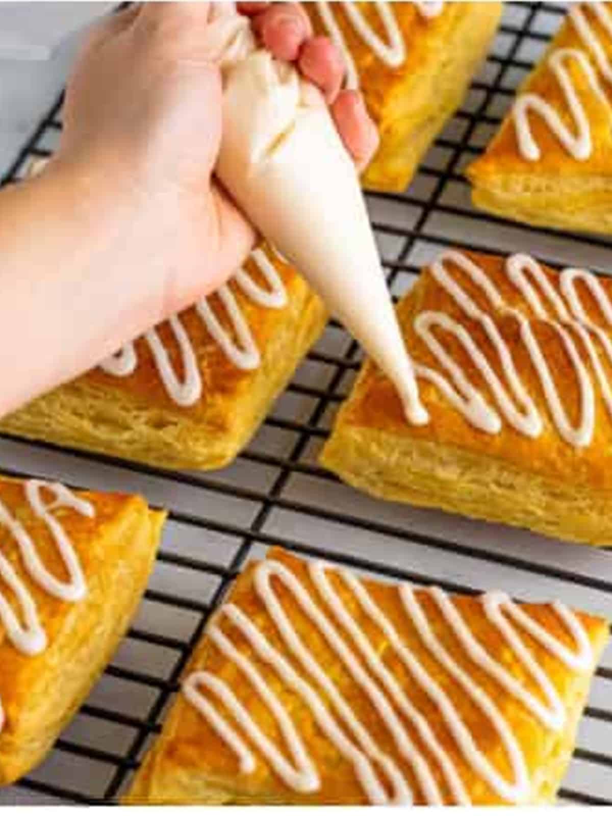 Piping zig zag lines of vanilla icing over baked toaster strudels on a wire rack.