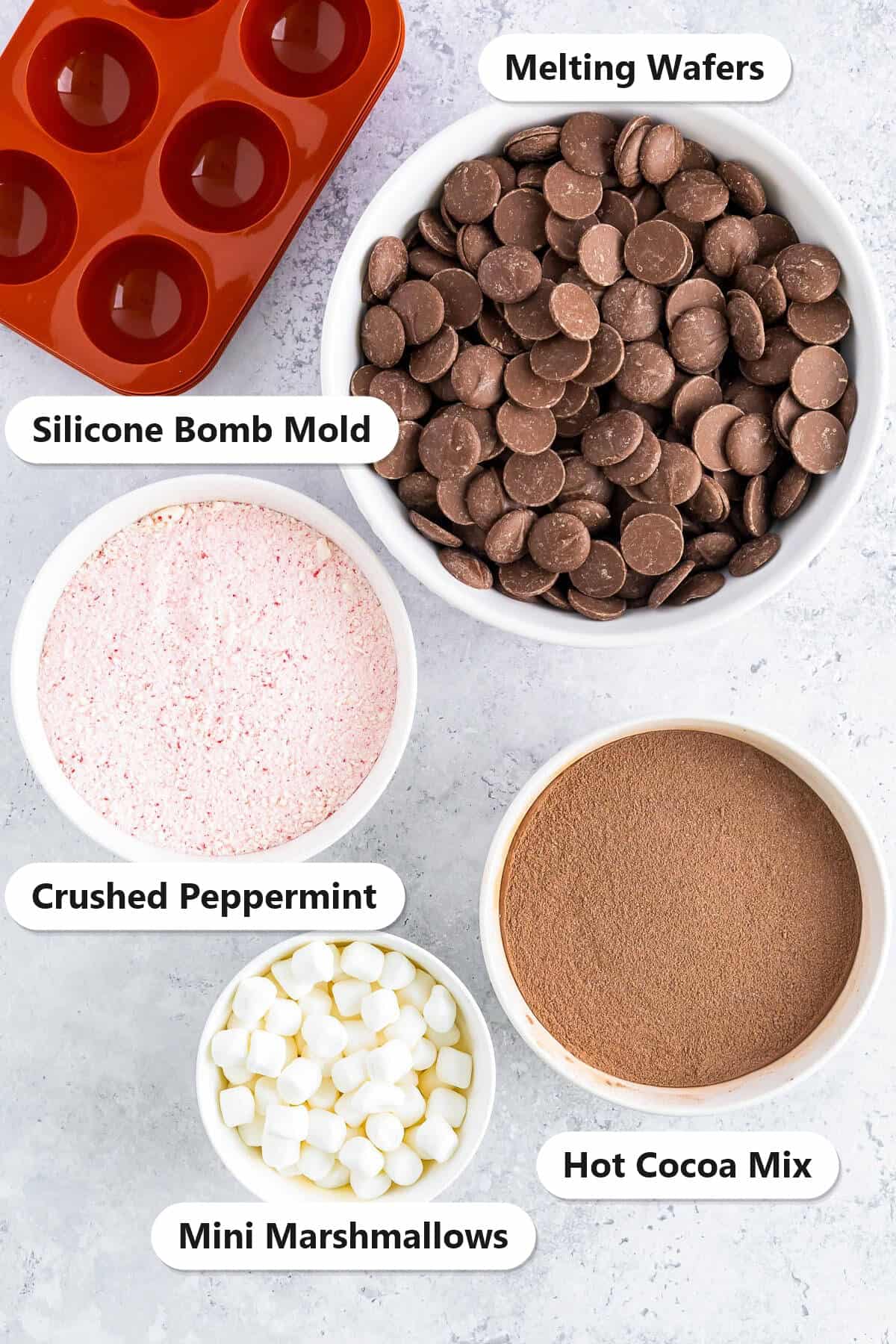 Labeled ingredients for Hot Cocoa Bombs including chocolate melting wafers, hot cocoa mix, crushed peppermint, mini marshmallows, and a silicone bomb mold.