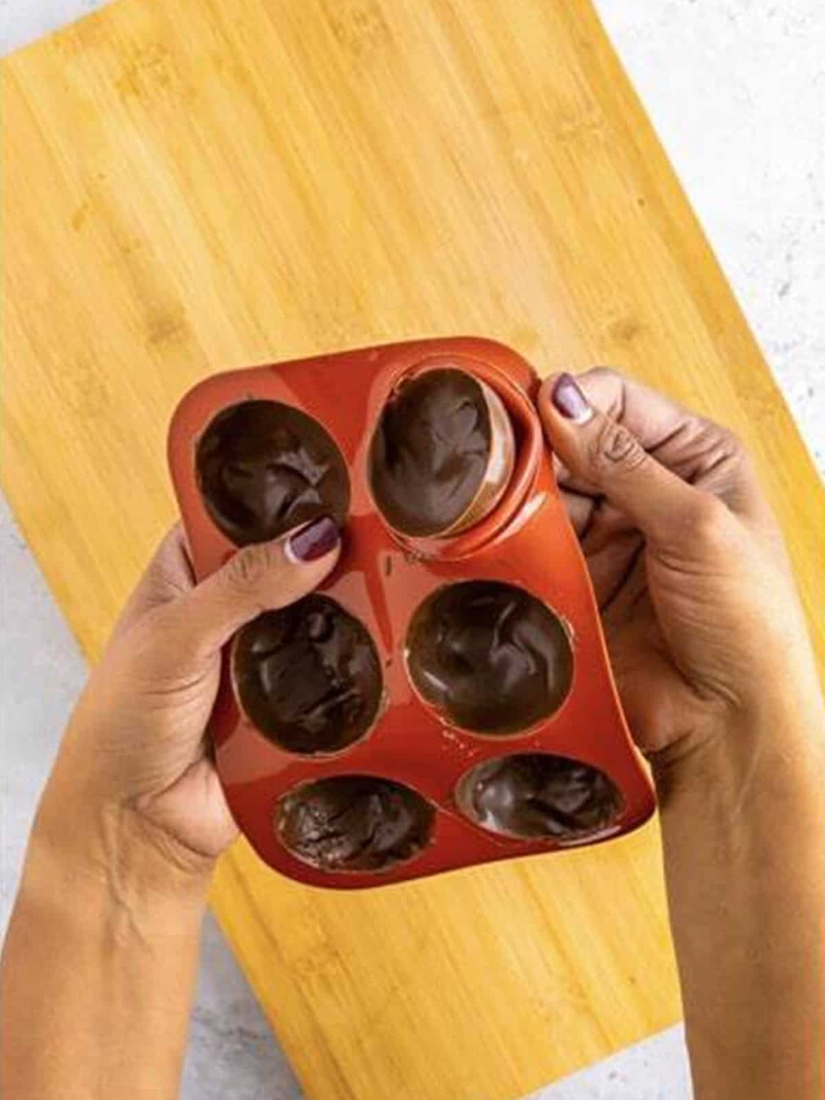 Hands gently peeling the silicone mold away from a hardened chocolate shell.