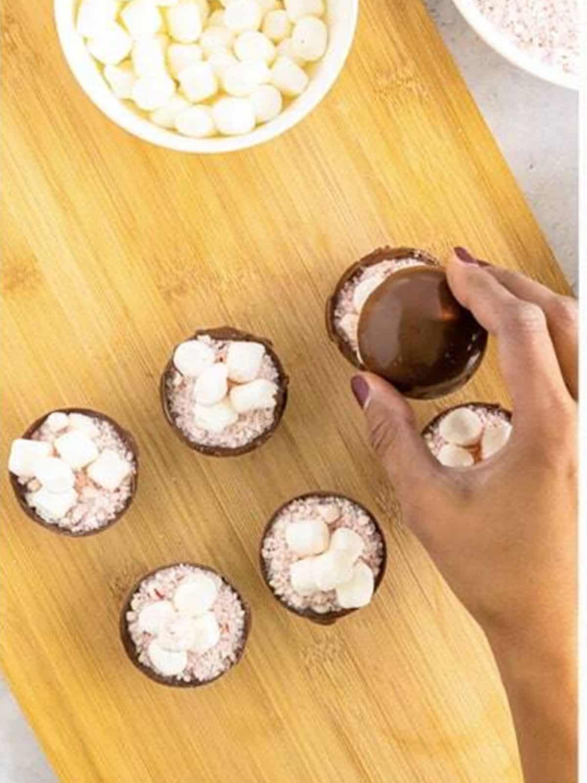 A hand placing the top chocolate shell onto a filled bottom shell to seal the hot cocoa bomb.