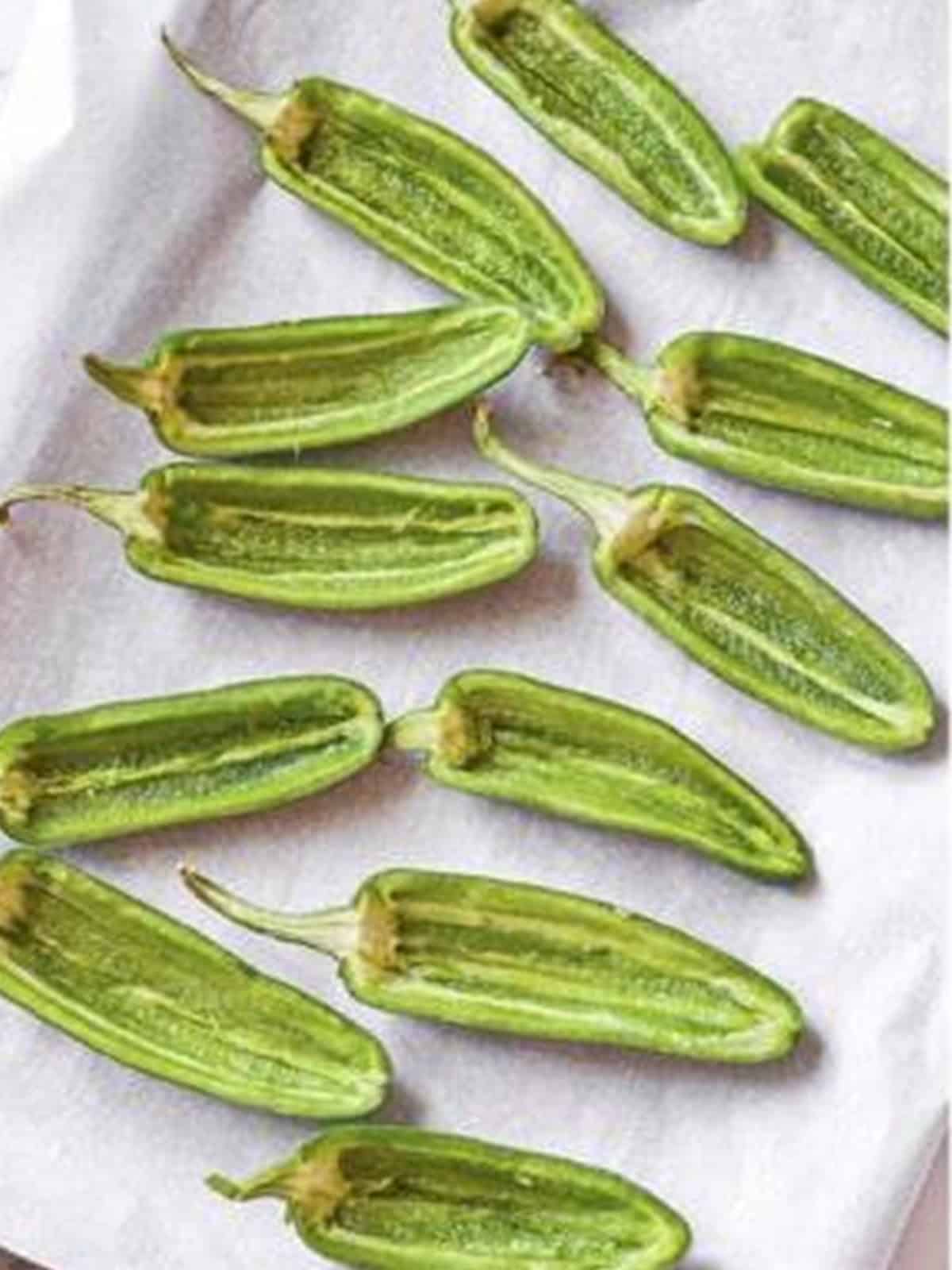 Halved and seeded jalapeno peppers on a parchment lined baking sheet.