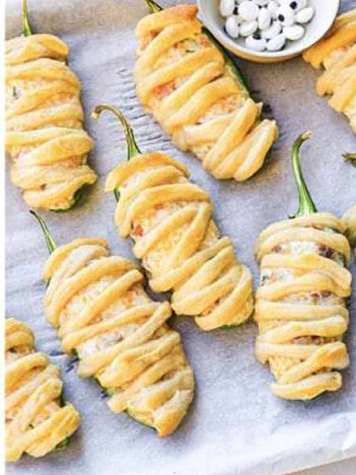 Baked Jalapeno Popper Mummies with candy eyes on a sheet tray.