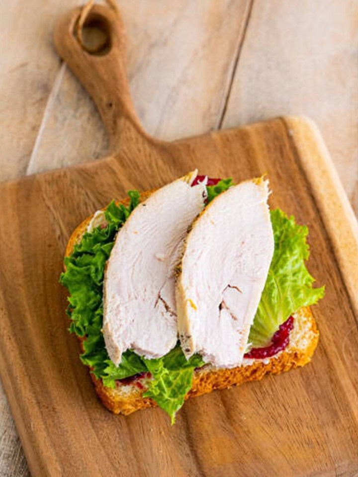 Sliced leftover turkey stacked on the lettuce for the leftover turkey sandwich.