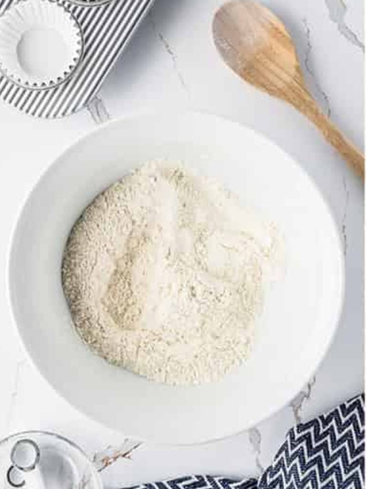 Flour, baking powder, and salt combined in a white bowl for Lemon Blueberry Cupcakes.
