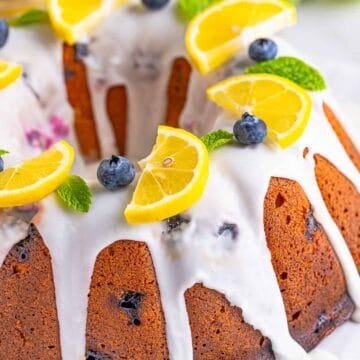 A whole Lemon Blueberry Pound Cake drizzled with lemon glaze and topped with lemon slices and fresh blueberries.