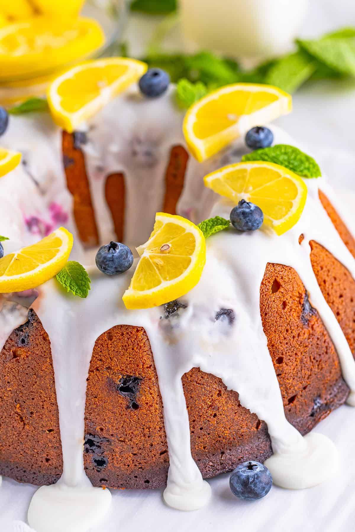 A whole Lemon Blueberry Pound Cake drizzled with lemon glaze and topped with lemon slices and fresh blueberries.
