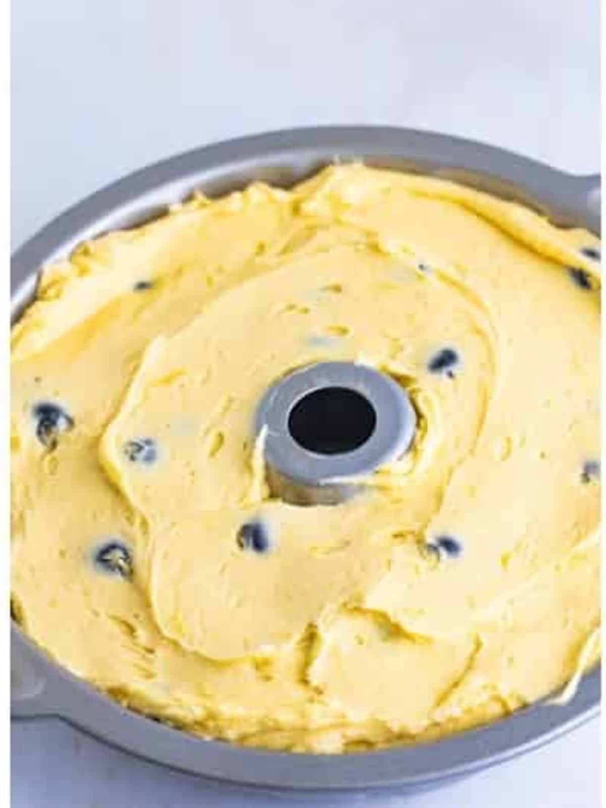 Spooning the blueberry pound cake batter into a greased bundt pan.