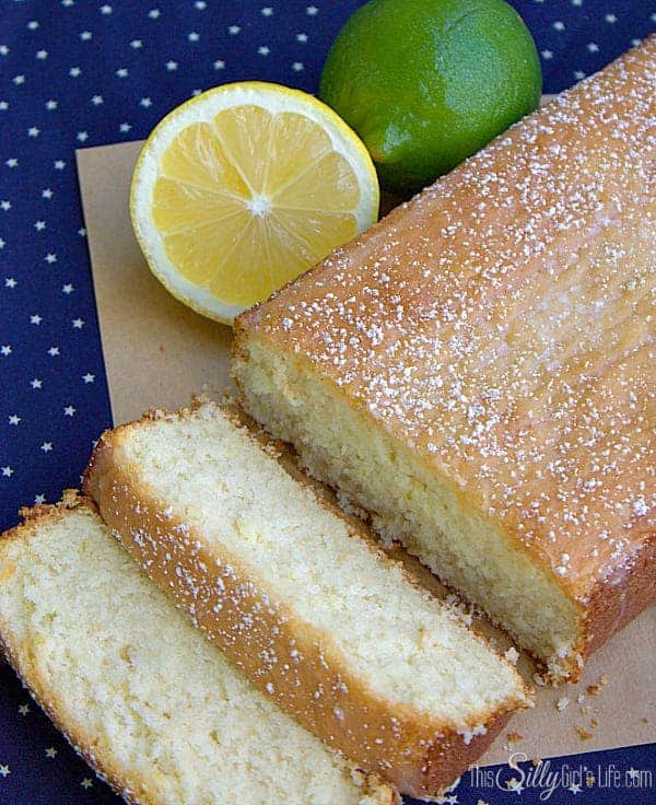 Close up of lemon lime cake slices dusted with powdered sugar next to fresh lemon and lime.