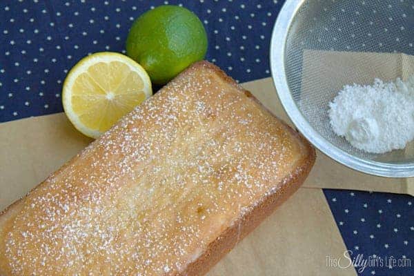 Whole glazed lemon lime cake with fresh lemon, lime, and a sifter of powdered sugar.