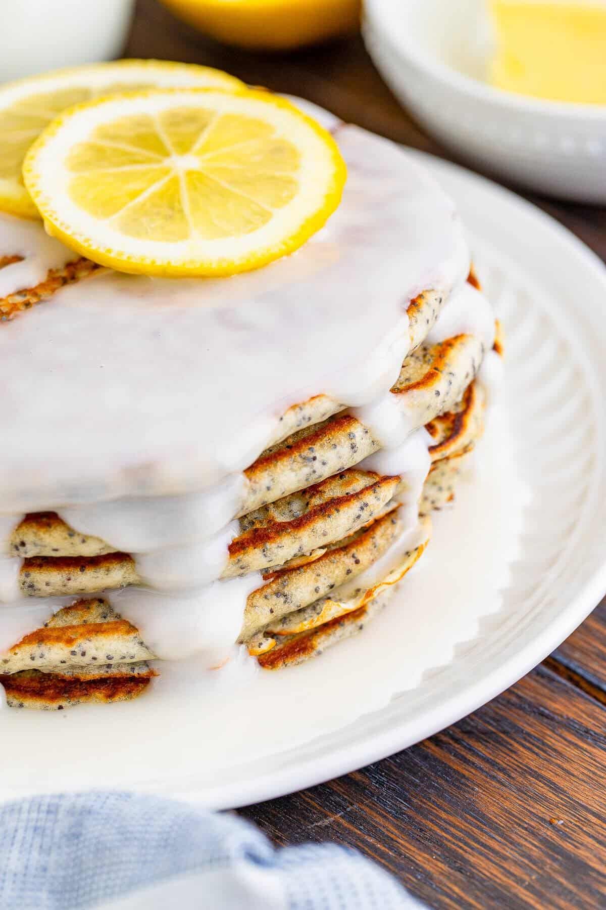 A fork lifting a bite from a stack of glazed lemon poppy seed pancakes showing the fluffy poppy seed flecked layers.