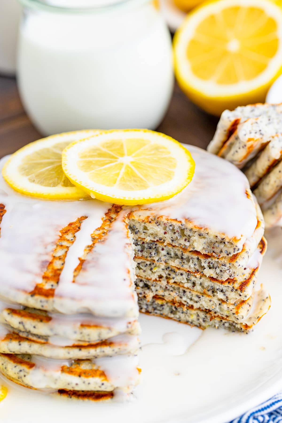 A tall stack of lemon poppy seed pancakes topped with a pat of butter and a lemon slice.
