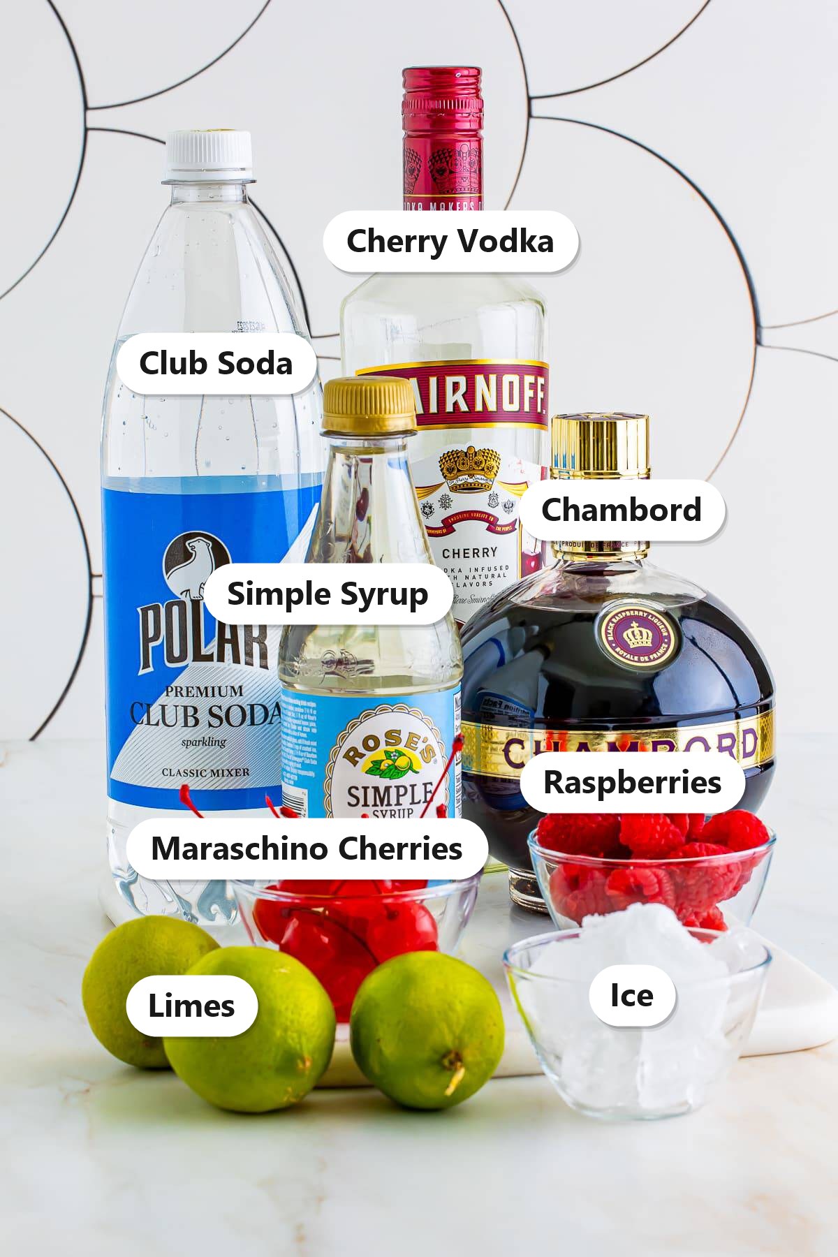 Labeled ingredients for a love potion cocktail including Chambord, cherry vodka, simple syrup, club soda, limes, raspberries, maraschino cherries, and ice.