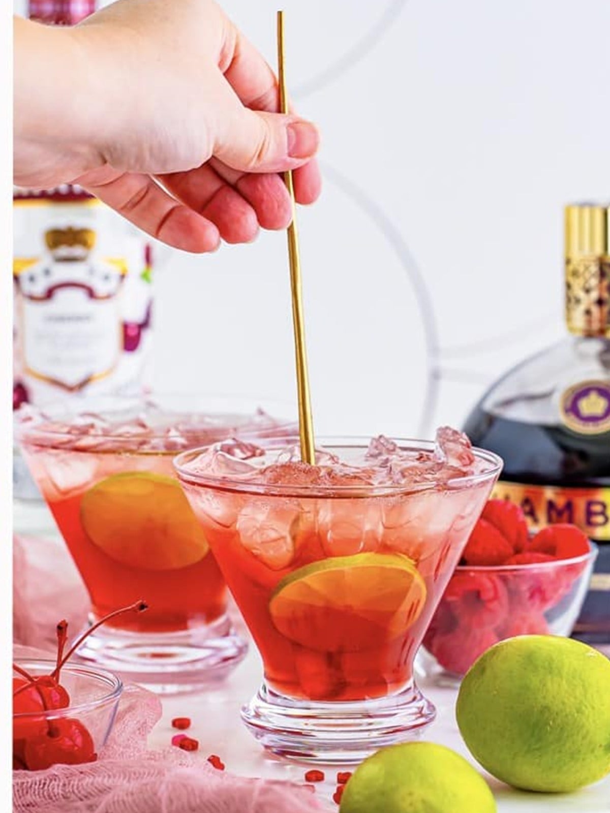 A love potion cocktail garnished with raspberries, a maraschino cherry, and a lime wheel.