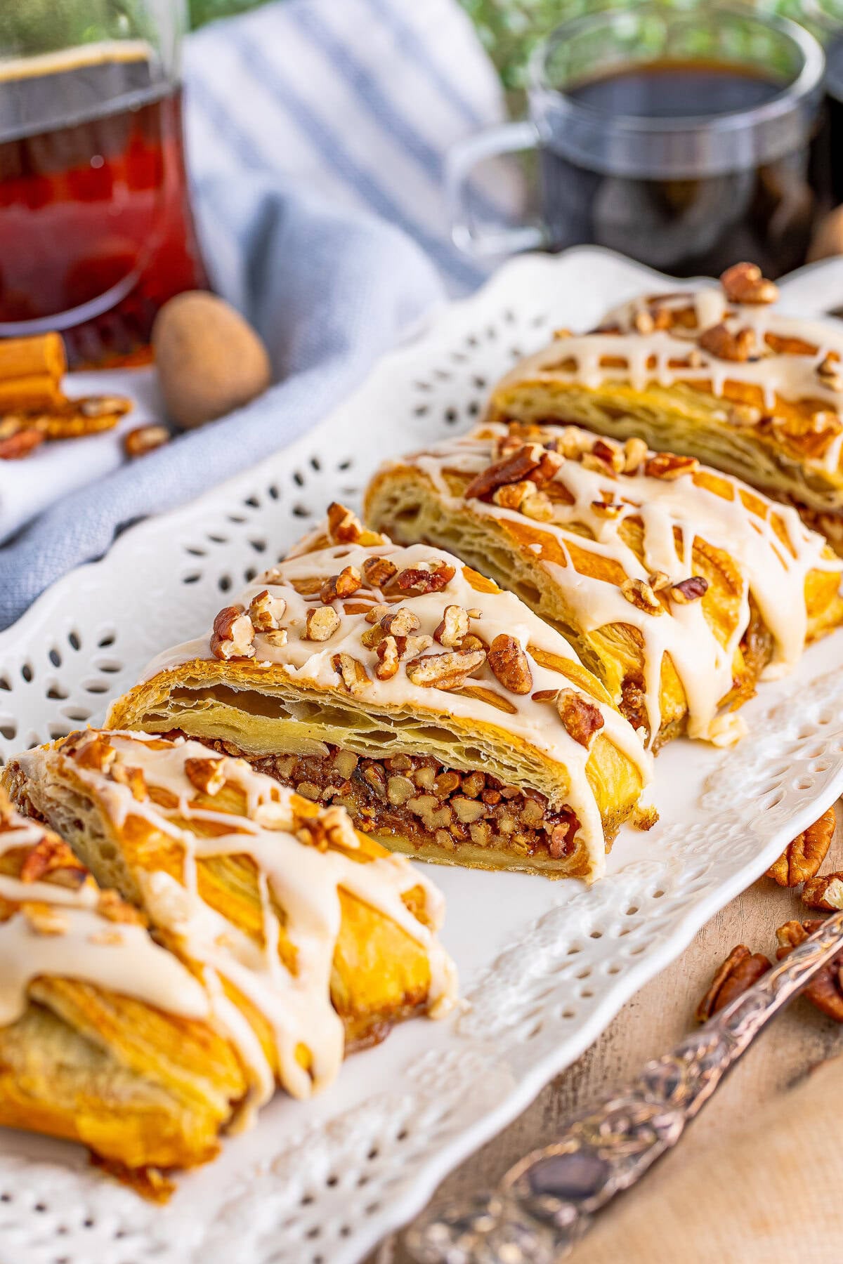 A Maple Pecan Pastry Braid on a white platter drizzled with maple glaze and topped with chopped pecans.