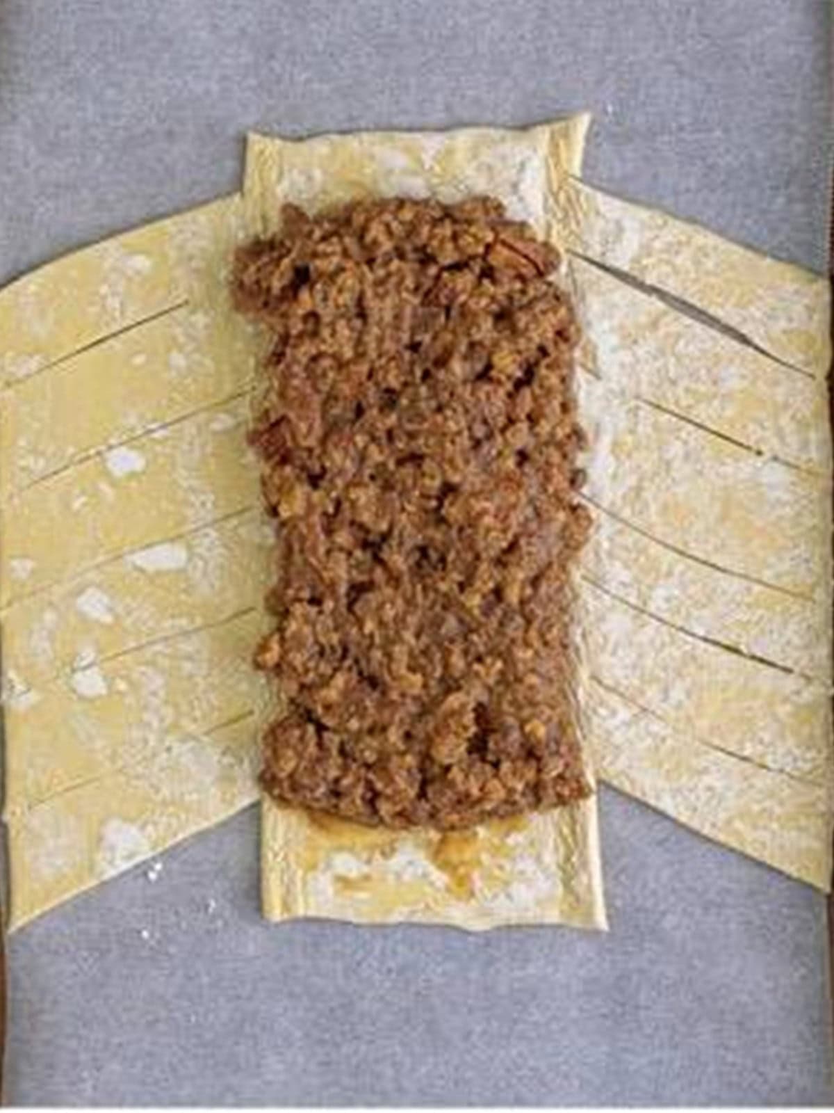Maple pecan filling spooned down the center of a puff pastry sheet with slits cut along both sides.