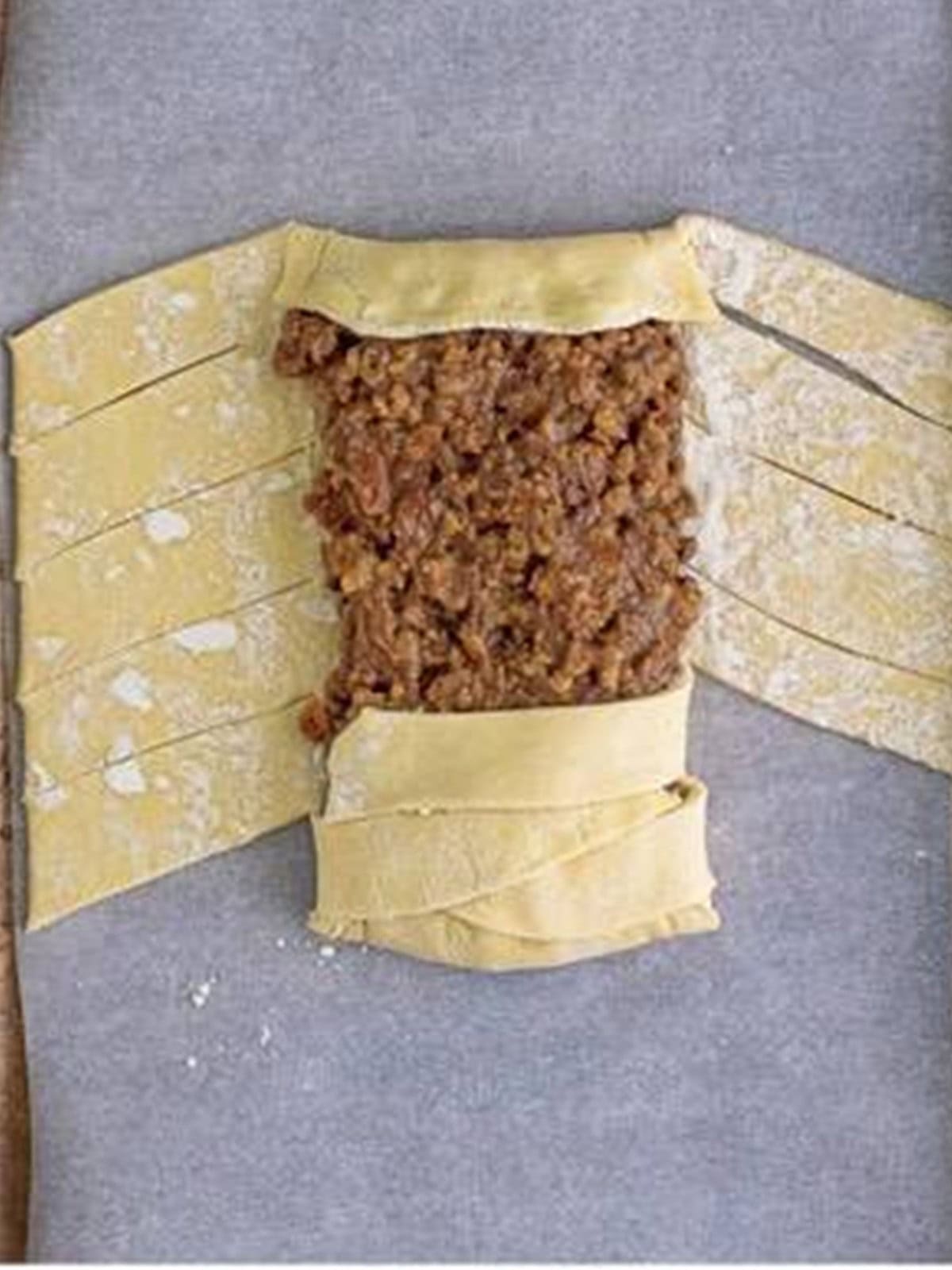 Folding the cut puff pastry strips over the maple pecan filling to form a braid.