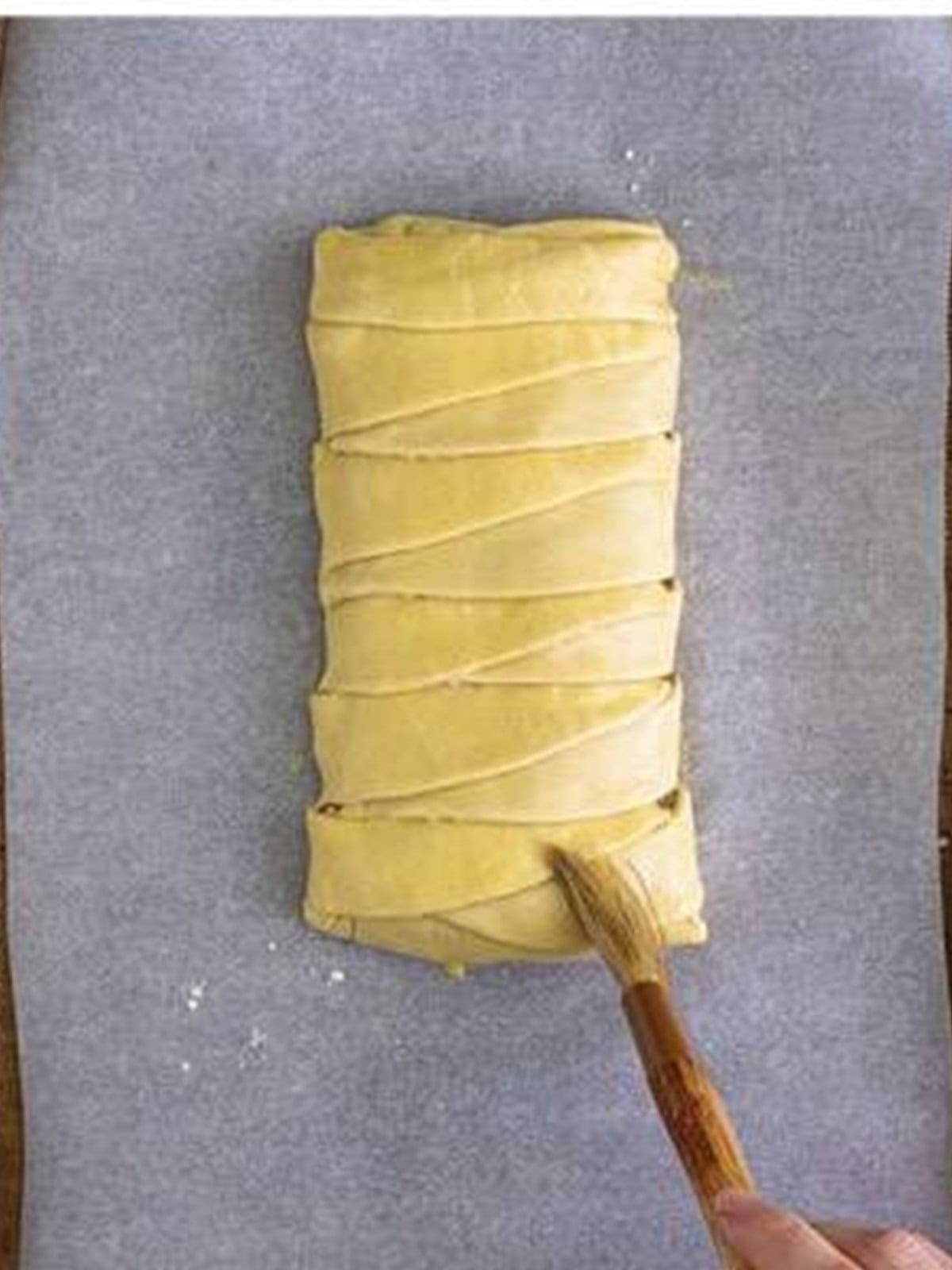 Brushing egg wash over the braided puff pastry before baking.