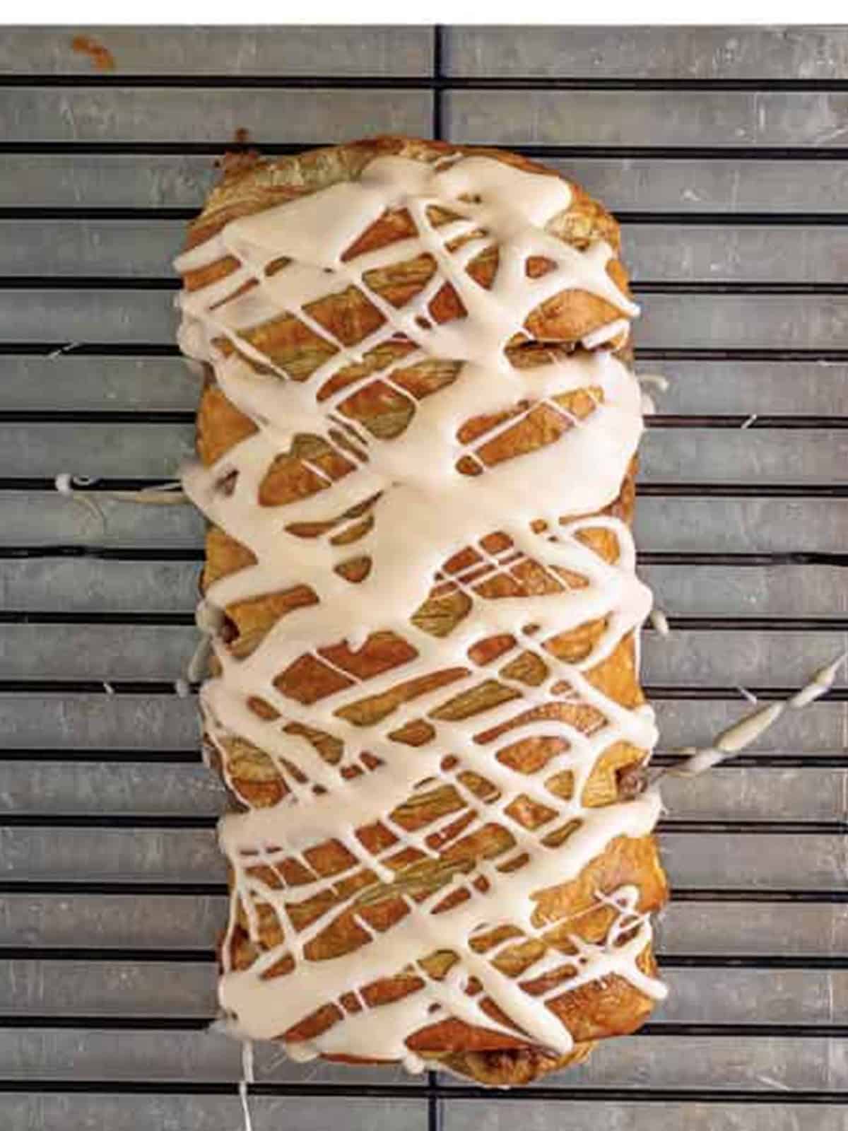 Drizzling maple glaze over the baked Maple Pecan Pastry Braid on a wire rack.