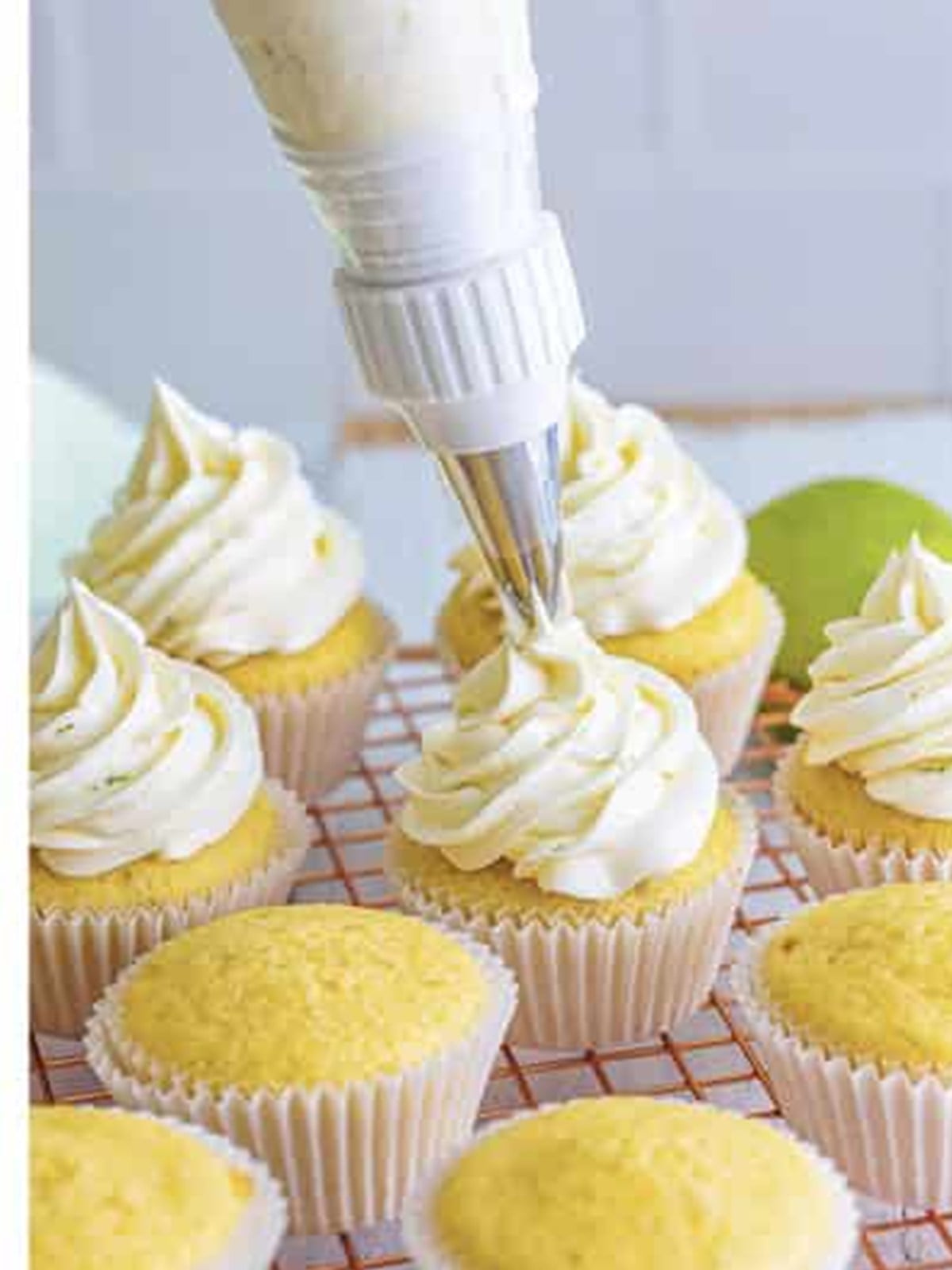 Piping tequila lime frosting swirls onto the cooled margarita cupcakes.