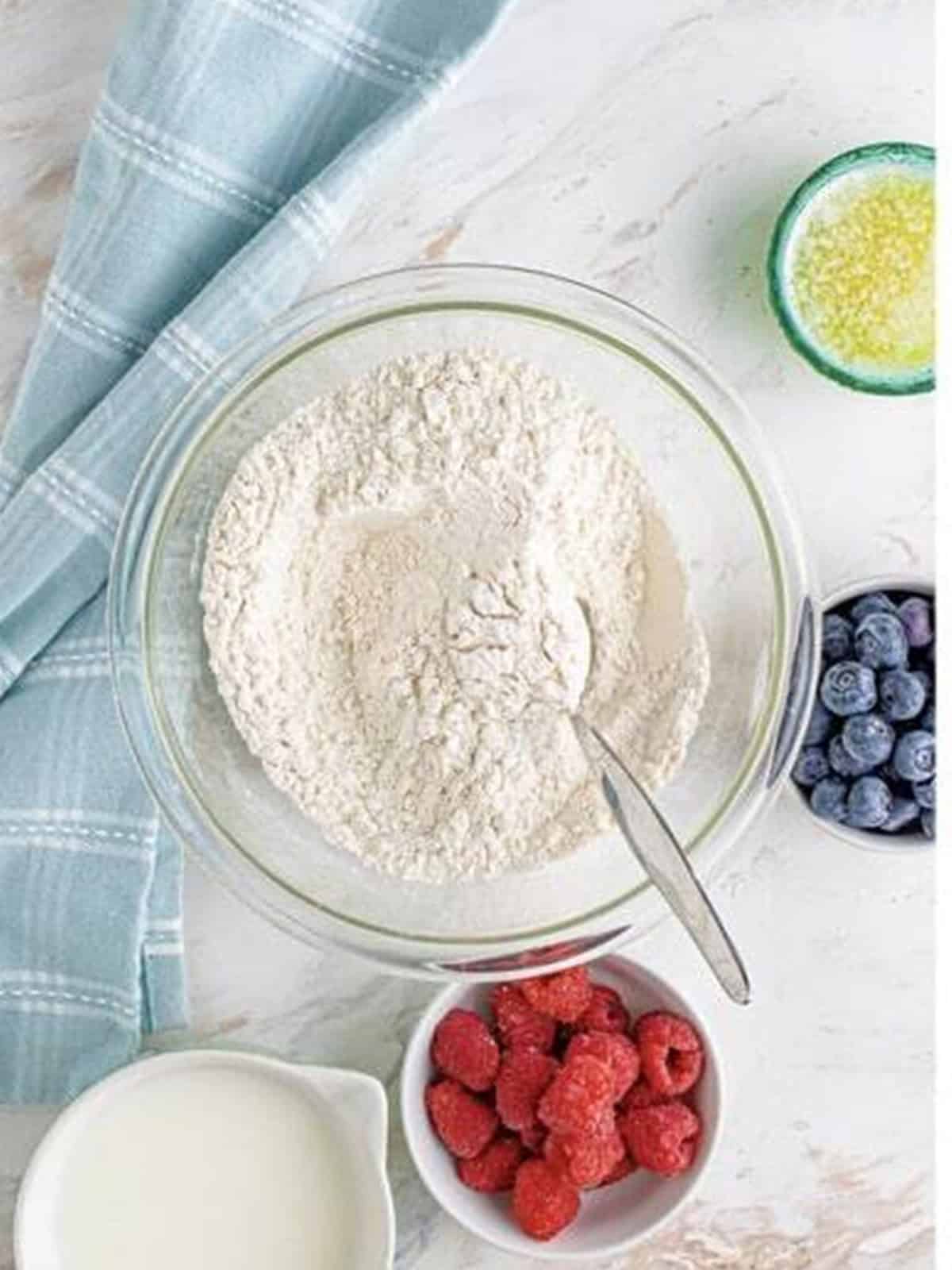 Flour, sugar, baking powder, and salt combined in a glass mixing bowl for mini berry pancake bites.