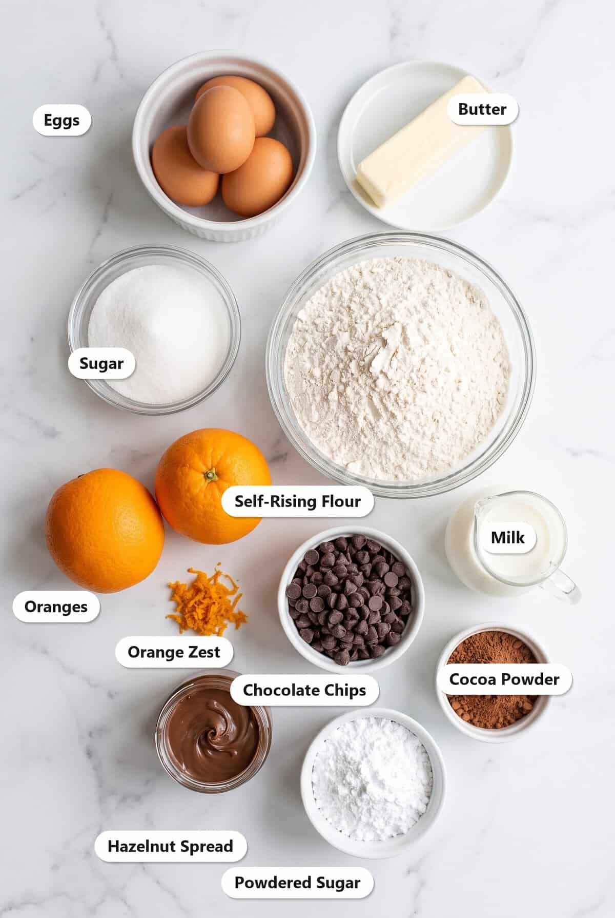 Labeled ingredients for Mini Bundt Cakes: eggs, butter, sugar, self-rising flour, oranges, orange zest, milk, chocolate chips, cocoa powder, hazelnut spread, and powdered sugar.