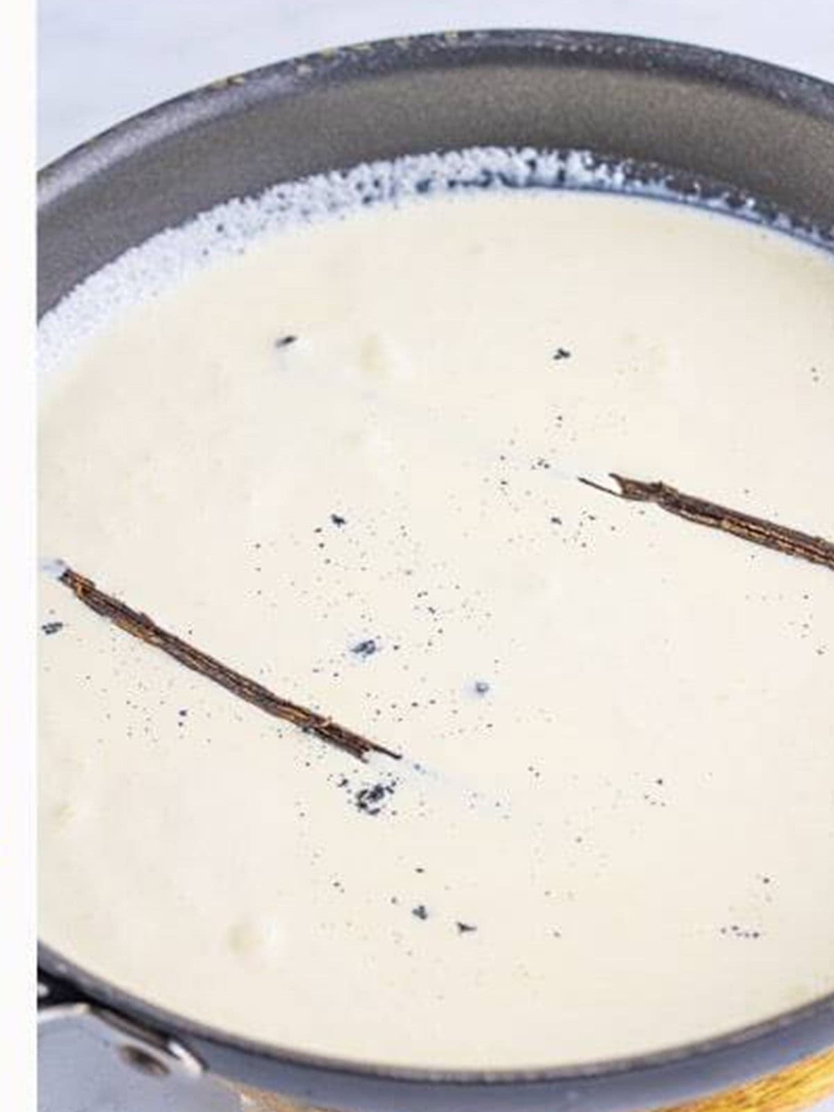 Heavy cream, sugar, and vanilla bean simmering in a saucepan for mini trifles.