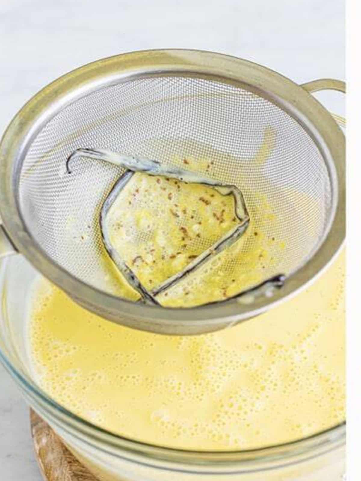 Straining the tempered custard through a fine mesh strainer into a bowl.