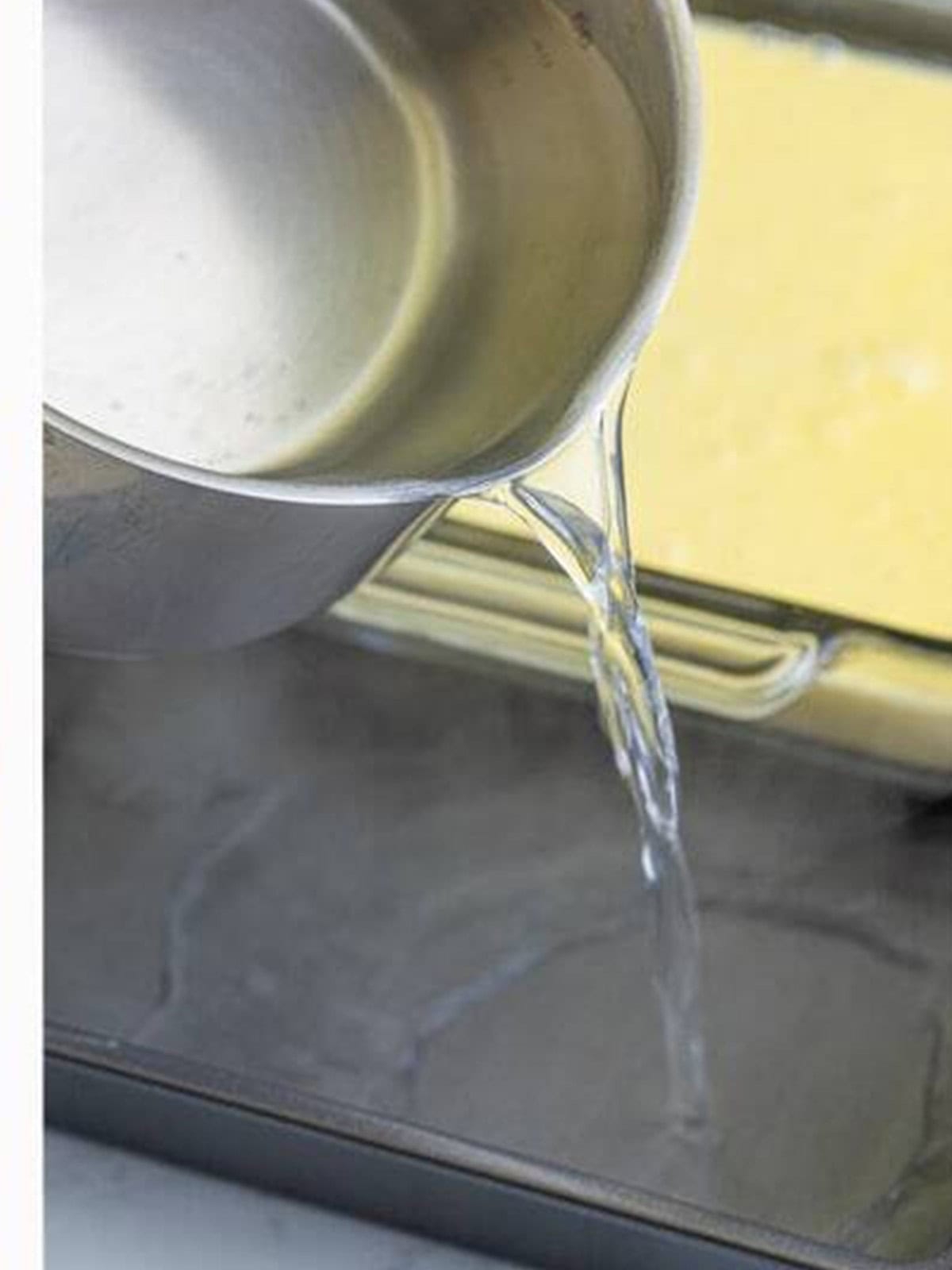 Pouring boiling water into the roasting pan around the custard dish for the water bath.