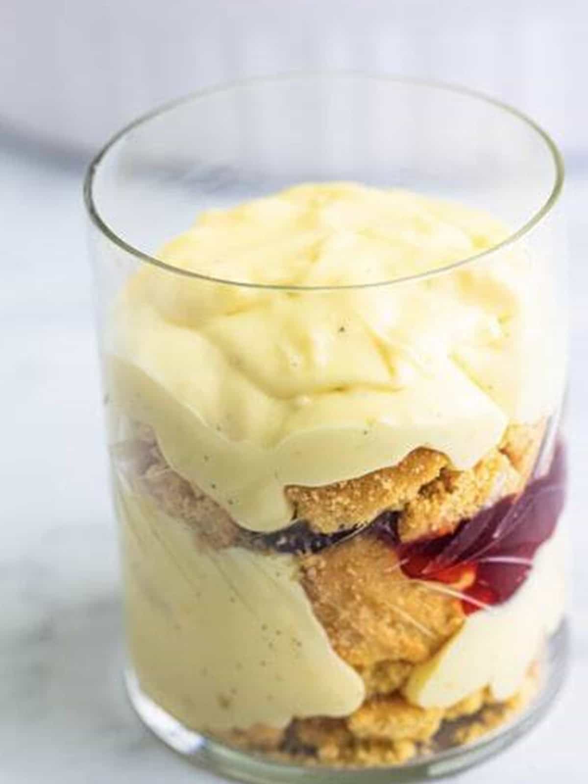 A glass layered with crushed shortbread cookies, vanilla custard, and raspberry jam for mini trifles.