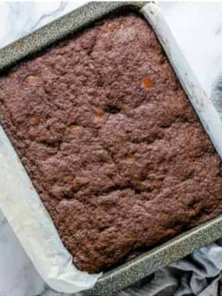 Baked brownie layer with a shiny set top cooling in the pan.