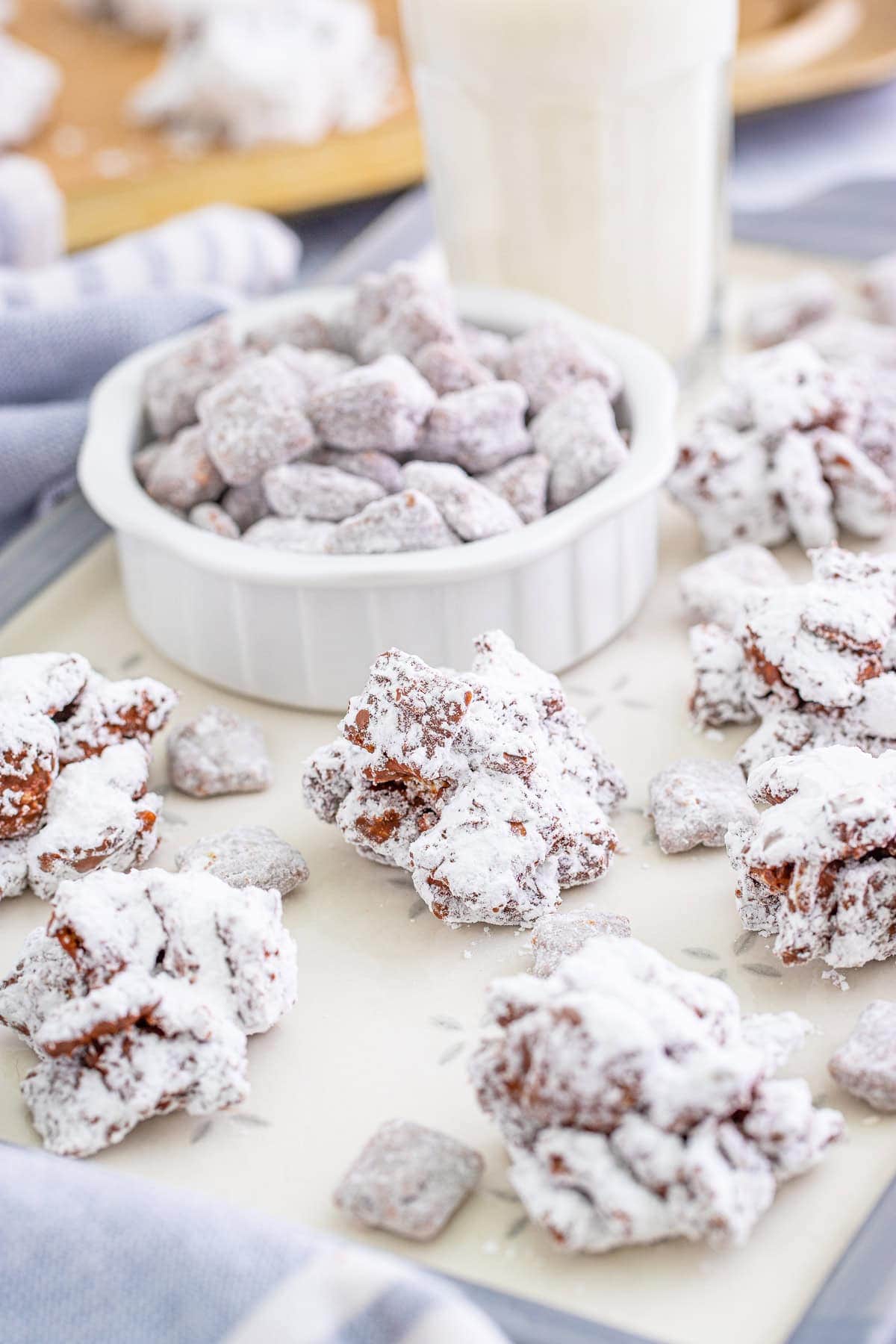 Muddy Buddy Cookies clusters served in a white bowl and scattered on a tray.