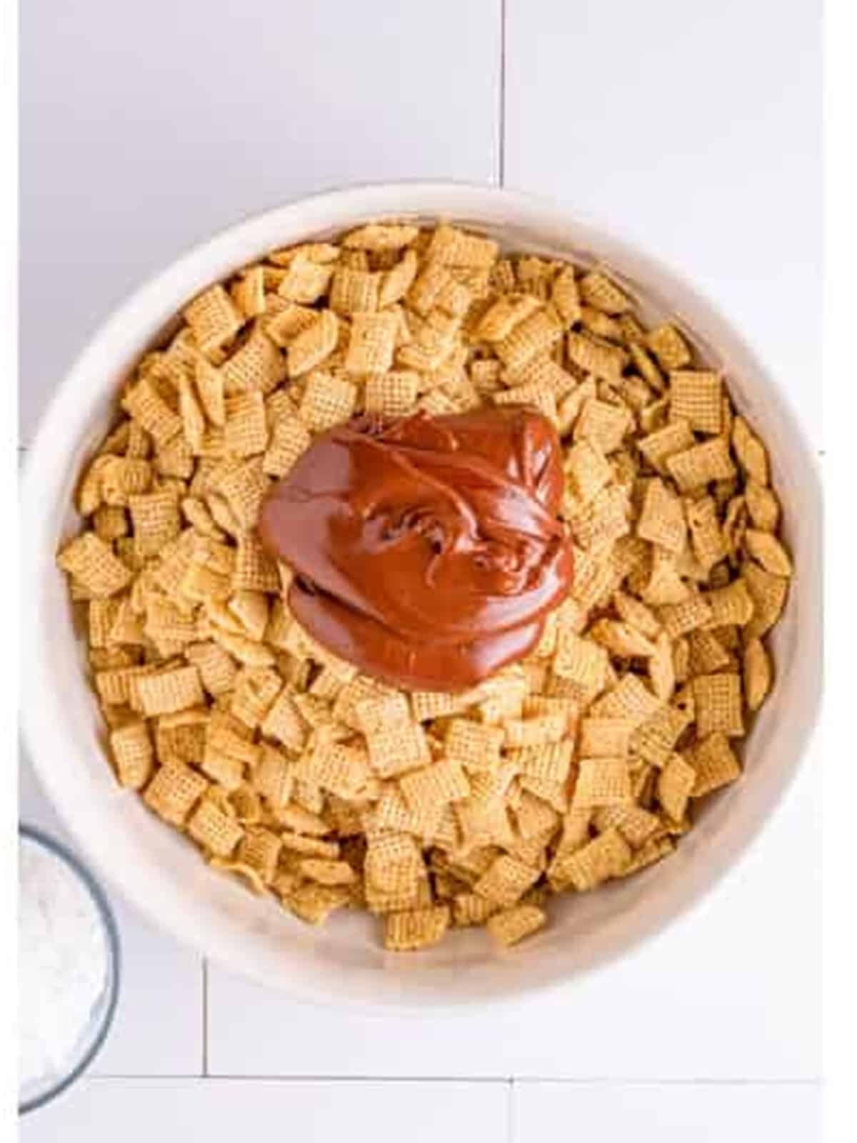Pouring the melted chocolate mixture over rice Chex cereal in a large bowl.