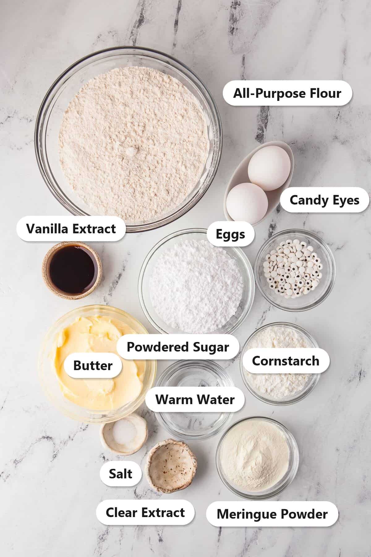 Labeled ingredients for mummy cookies including all-purpose flour, butter, powdered sugar, eggs, vanilla extract, cornstarch, salt, meringue powder, warm water, clear extract, and candy eyes.