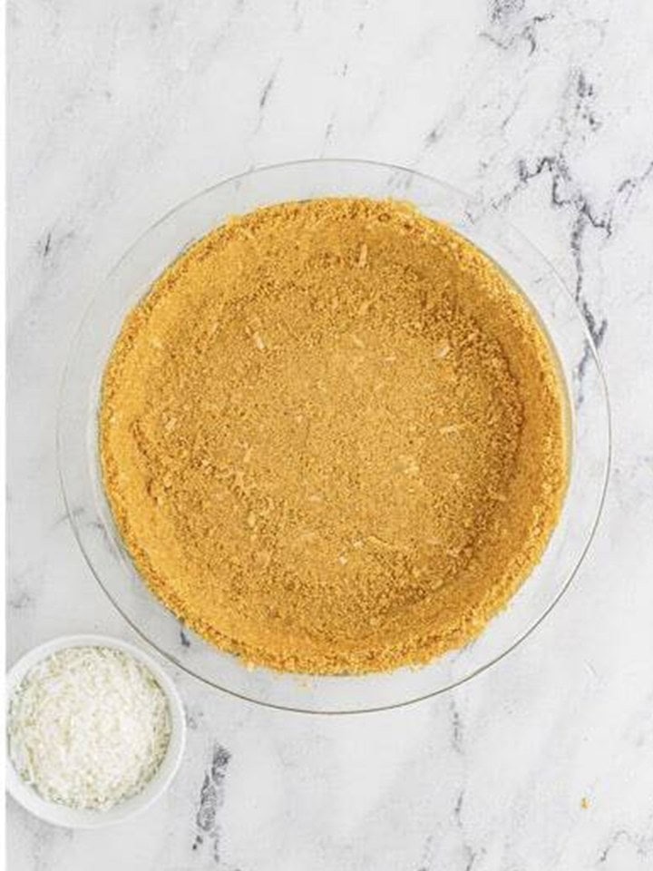 The crust pressed into the bottom and sides of a glass pie plate for no bake coconut cream pie.