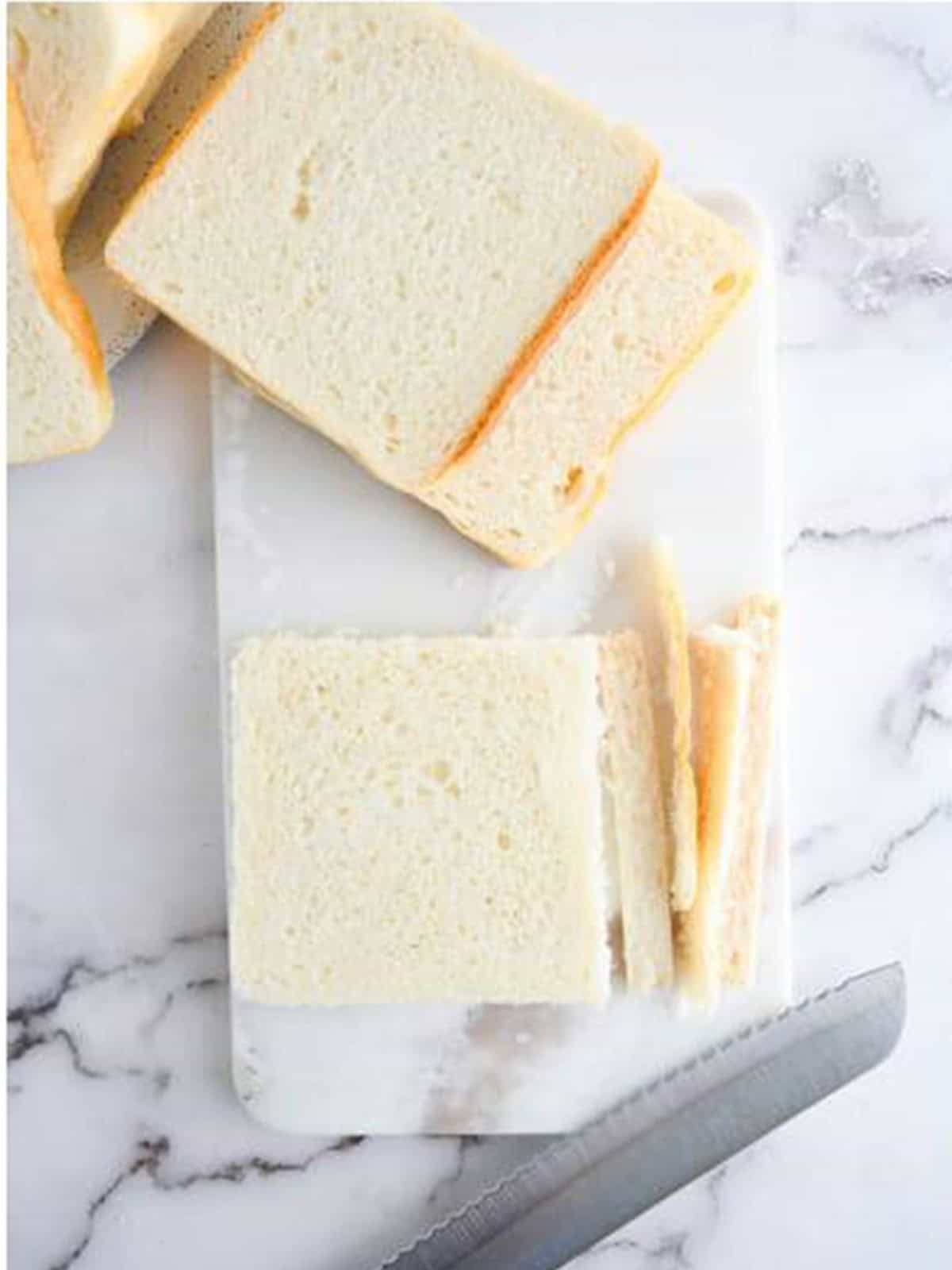 Slices of bread with crusts cut off on a cutting board for Nutella French toast sticks.
