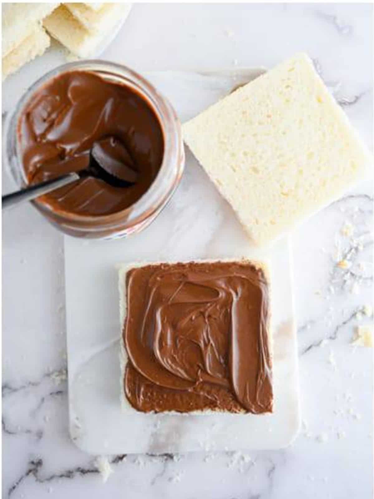 Nutella spread evenly over a slice of bread on a cutting board.