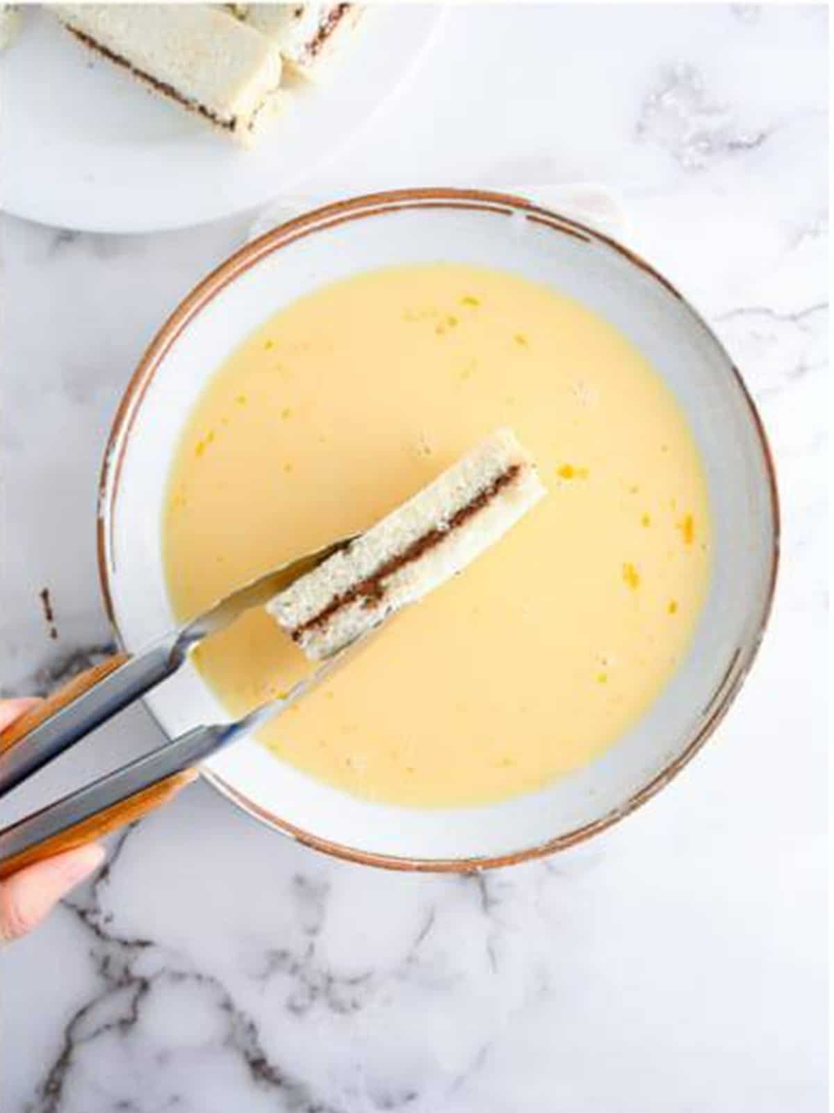 A Nutella stuffed French toast stick being dipped into an egg and milk mixture.