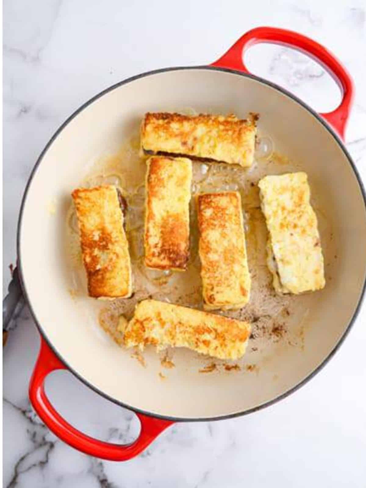 Nutella French toast sticks cooking golden brown in a skillet.