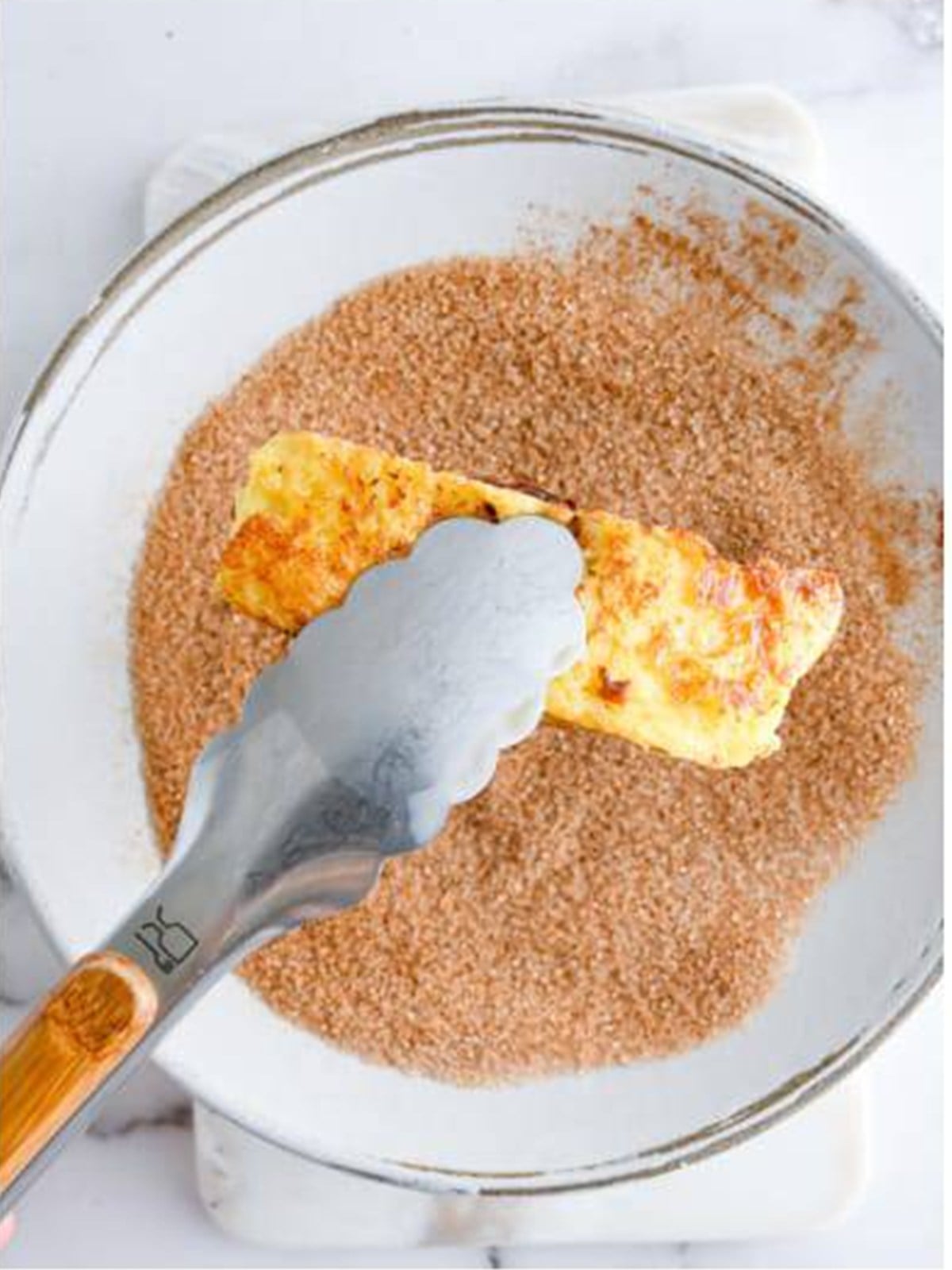 A cooked French toast stick being rolled in cinnamon sugar coating.