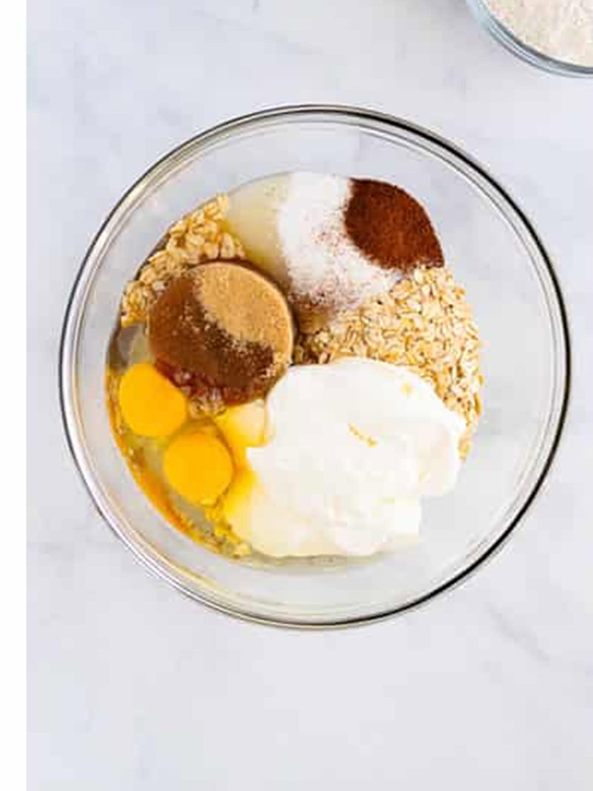 Eggs, sour cream, sugars, oats, and maple syrup in a bowl for oatmeal muffins.