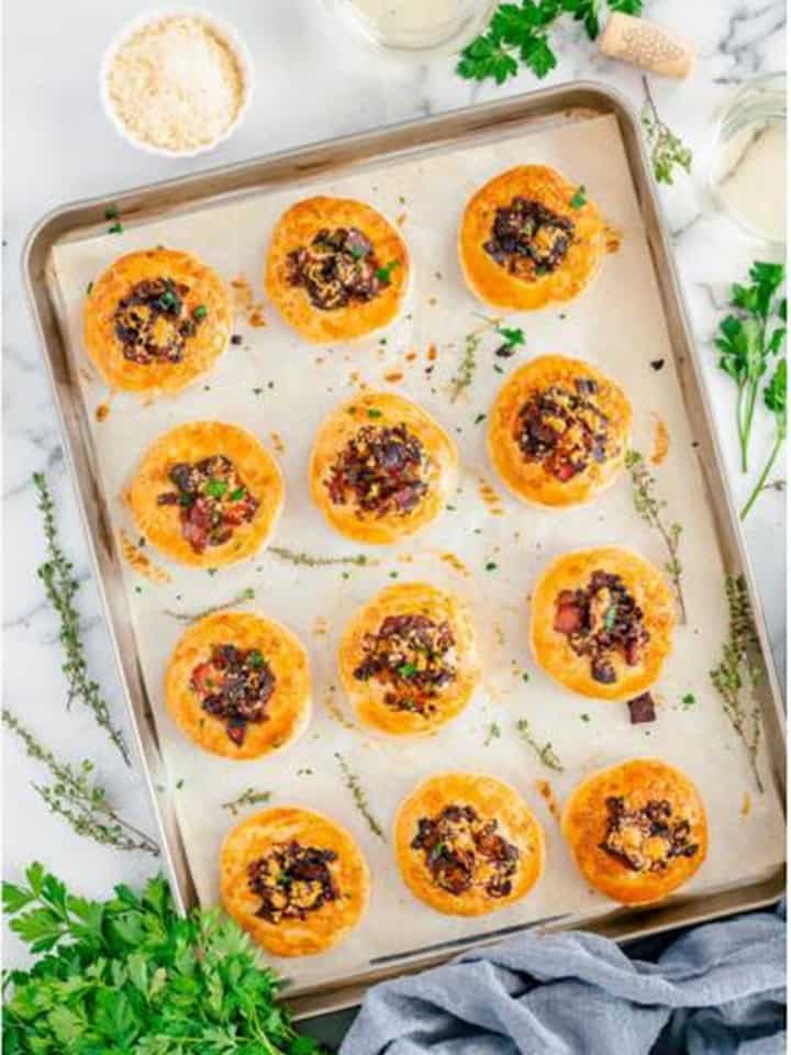 Golden baked mini Onion Tart bites on the sheet tray garnished with herbs.