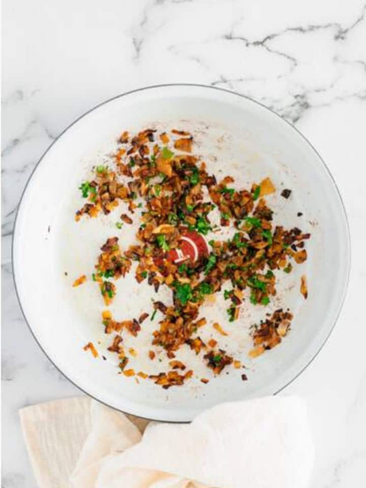 Deeply caramelized onions with bacon and fresh herbs stirred together in the pan.