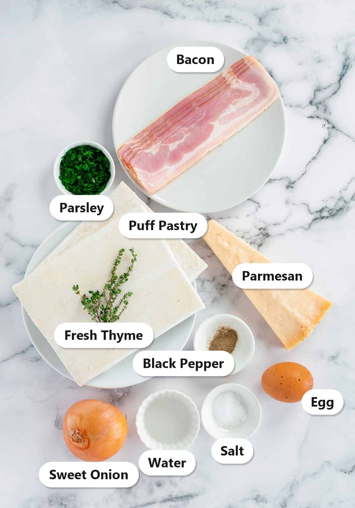 Labeled ingredients for mini Onion Tart bites including puff pastry, bacon, sweet onion, Parmesan, fresh thyme, parsley, egg, salt, pepper, and water.