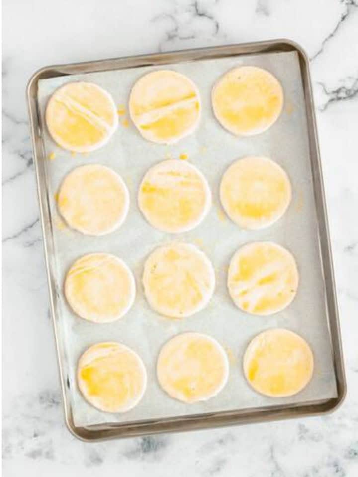 Puff pastry rounds brushed with egg wash on a parchment lined sheet tray.