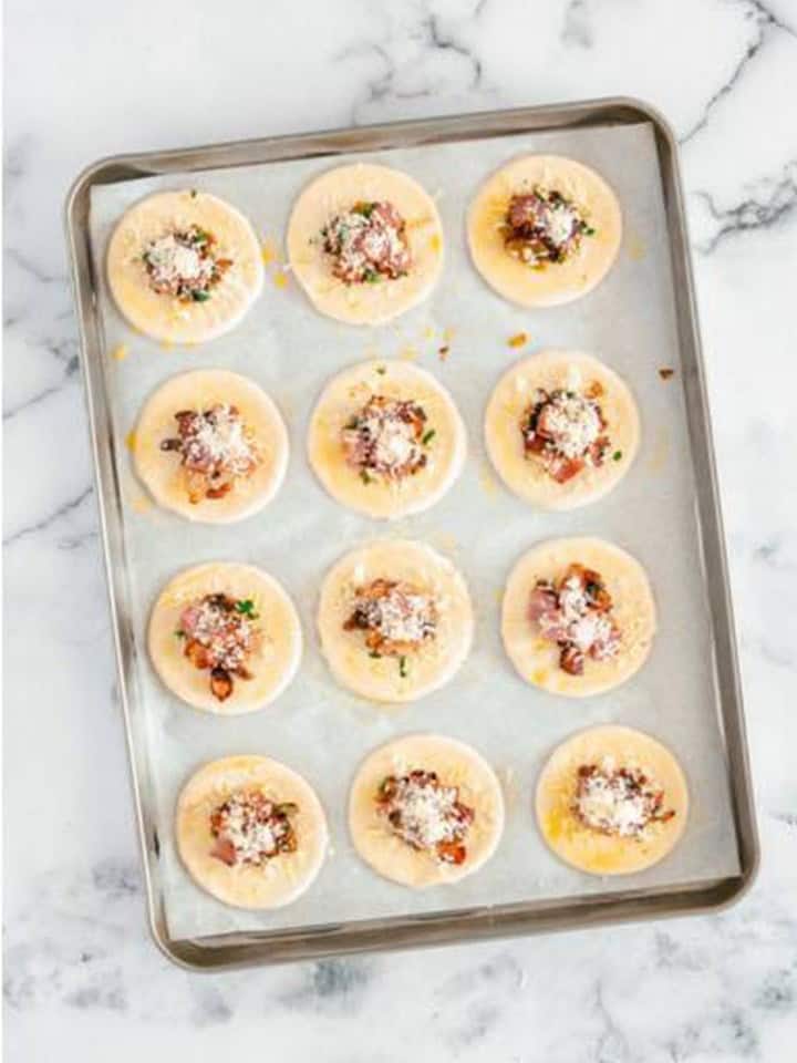 Pastry rounds topped with caramelized onions, bacon, and Parmesan before baking.
