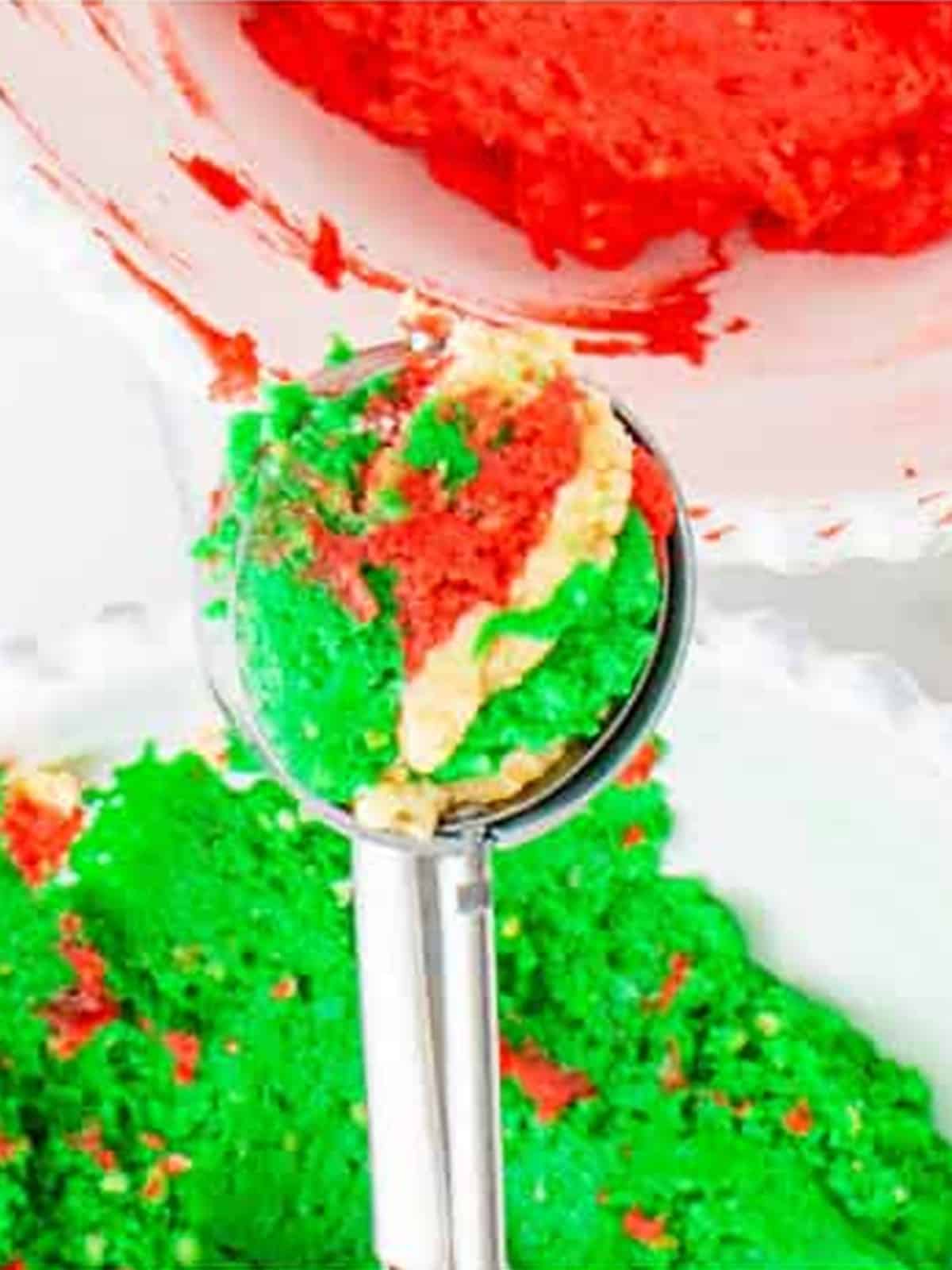 Cookie scoop layering red, green, and plain Oreo Balls mixture together.