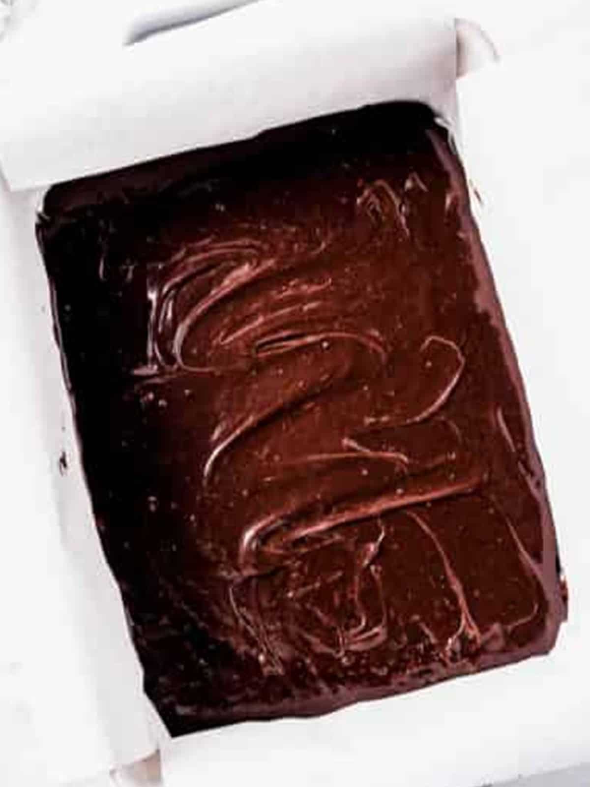 Brownie batter spread evenly in a parchment-lined baking pan for Oreo Brownies.