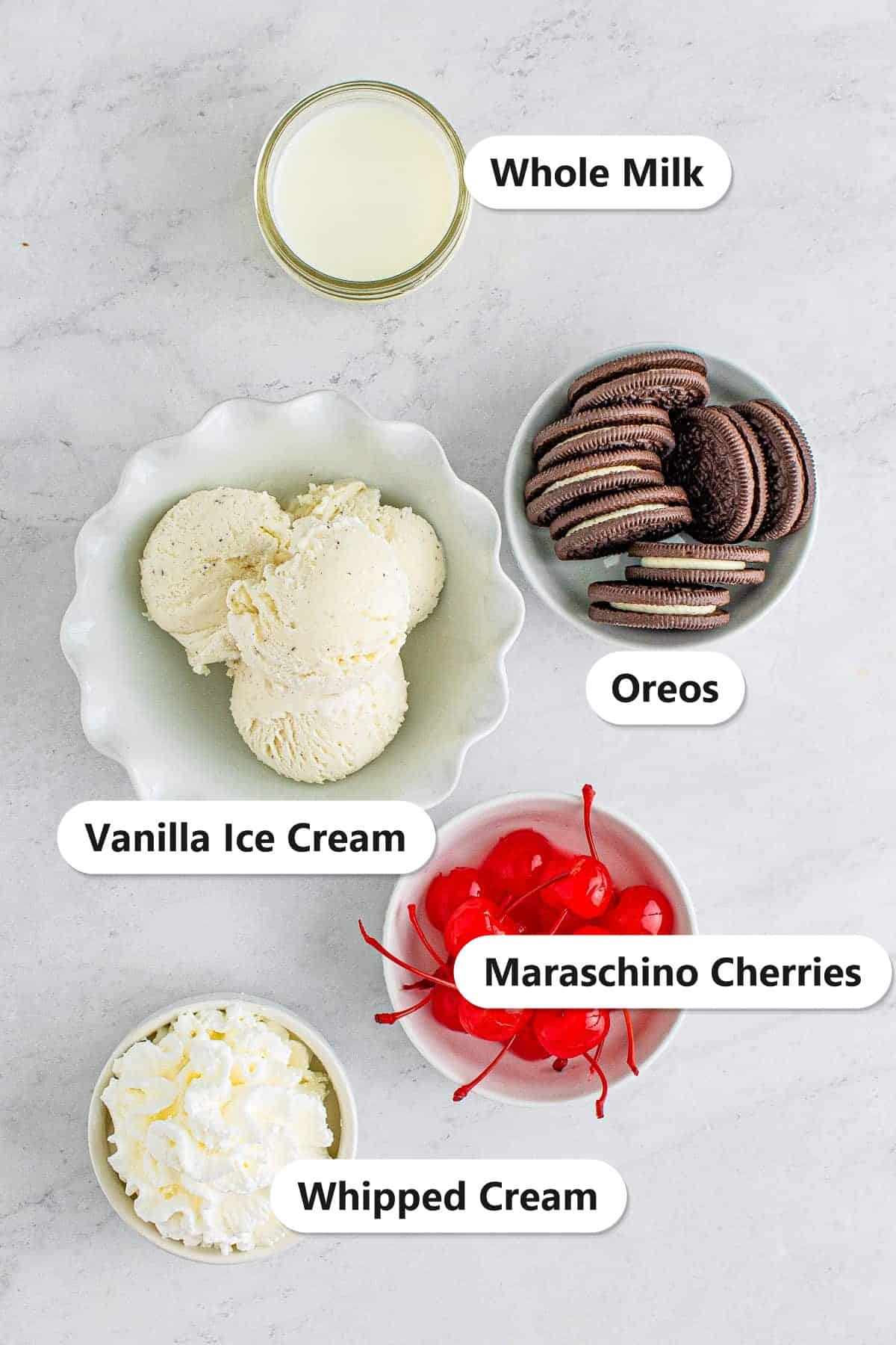 Labeled ingredients for an Oreo Milkshake including chocolate sandwich cookies, vanilla ice cream, whole milk, whipped cream, and maraschino cherries.