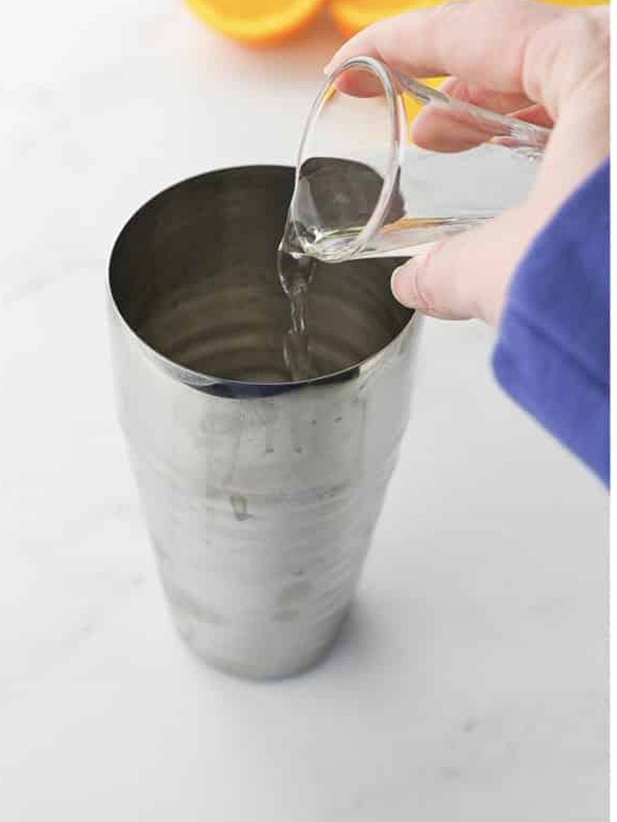 Pouring white rum from a shot glass into a cocktail shaker for a painkiller cocktail.